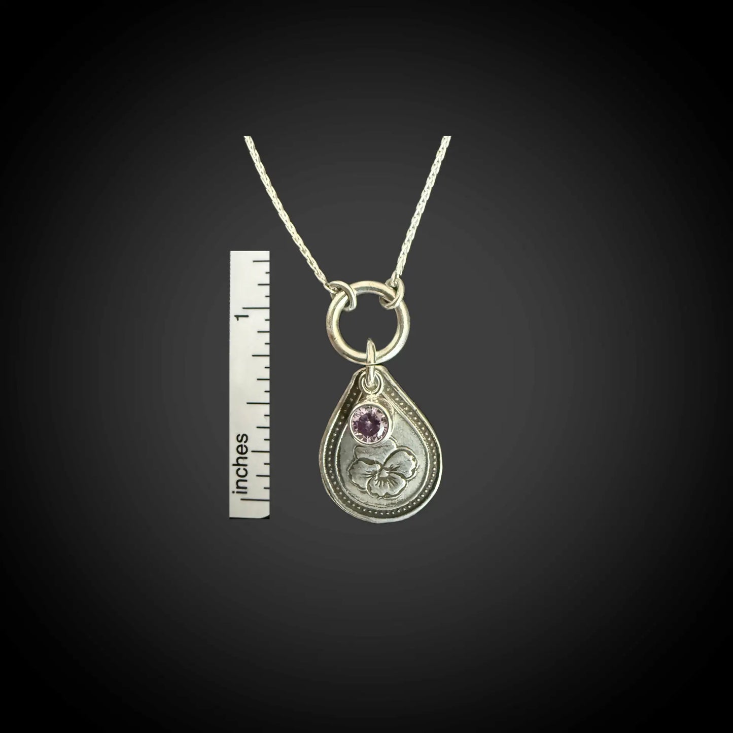 Size reference of February violet birth flower sterling silver necklace with amethyst-purple CZ stone next to inch ruler.