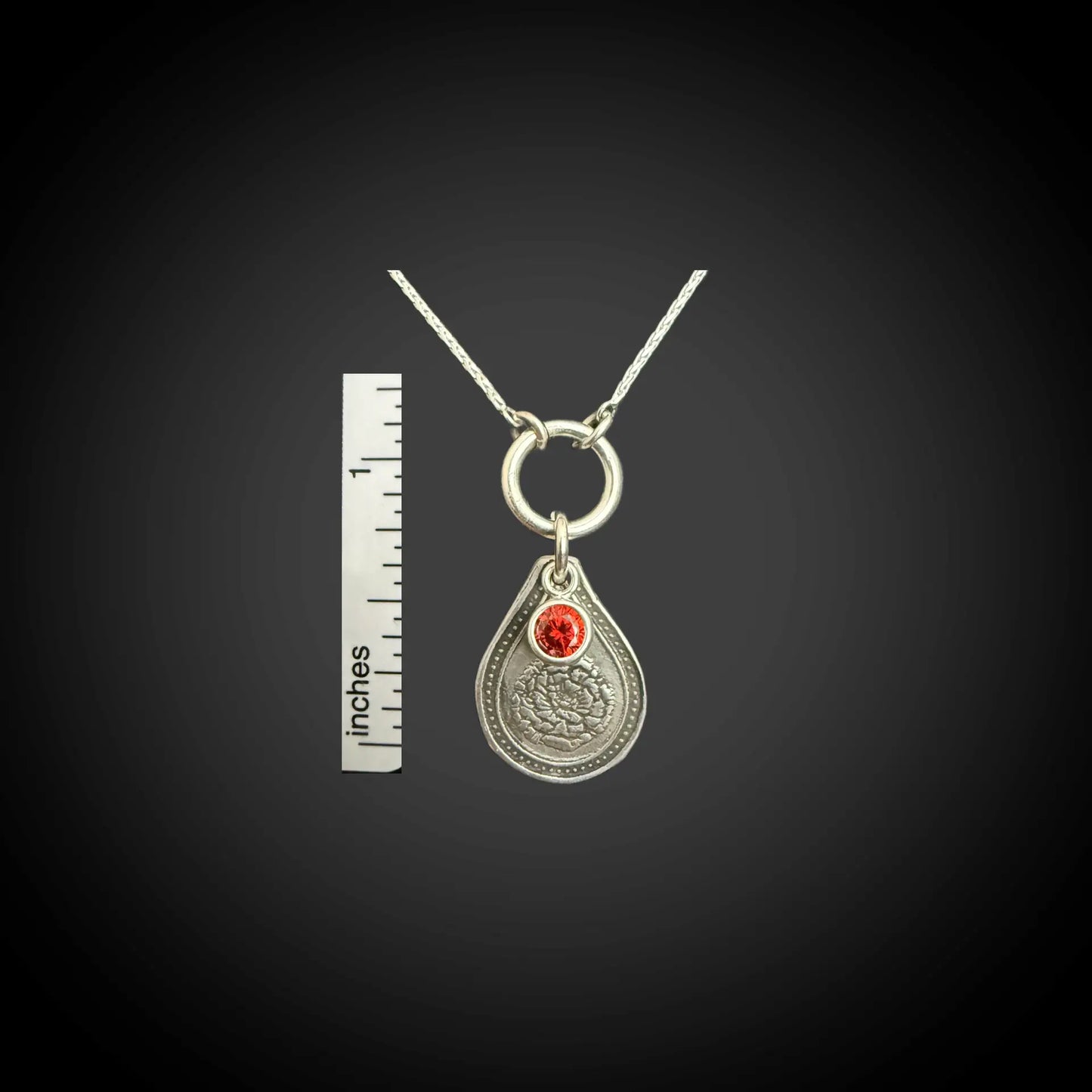 Size reference of January carnation birth flower sterling silver necklace with garnet-red CZ birthstone next to inch ruler.
