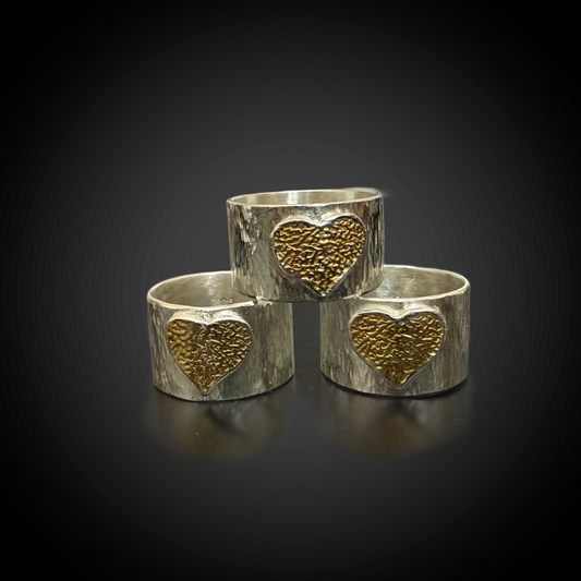 Three silver rings with gold heart designs on a black background