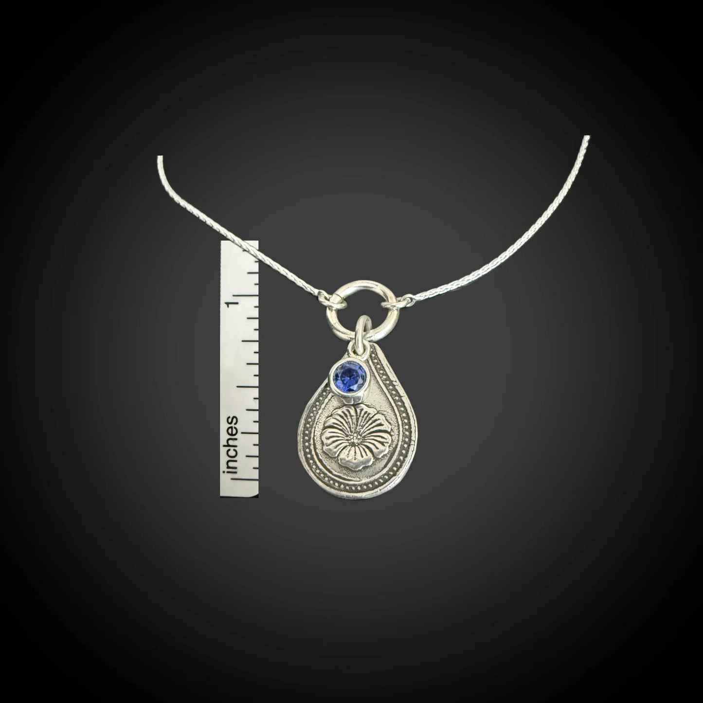 Size reference of September morning glory birth flower sterling silver necklace with sapphire-blue CZ stone next to inch ruler.