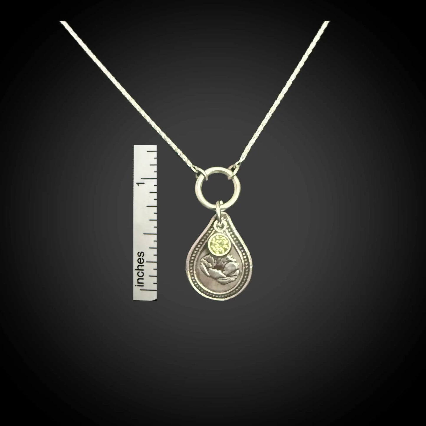 Size reference of August poppy birth flower sterling silver necklace with peridot-green CZ stone next to inch ruler.