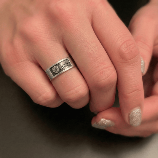 Close-up of a hand wearing a silver ring with a February violet birth month flower design.