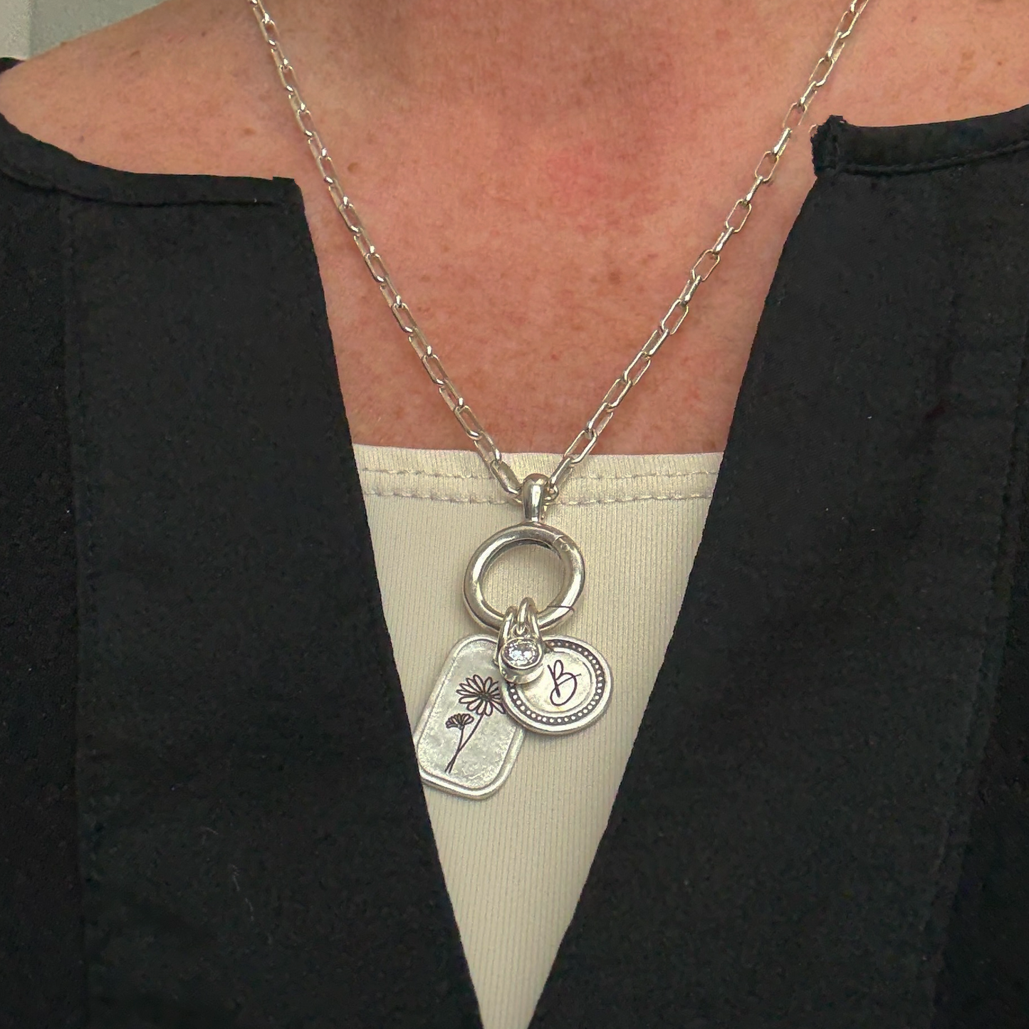 Silver necklace with charms worn by a person against a black and white background