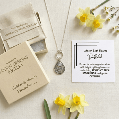 Silver necklace with pendant in Adorn Designs jewelry box, surrounded by daffodils on a light background