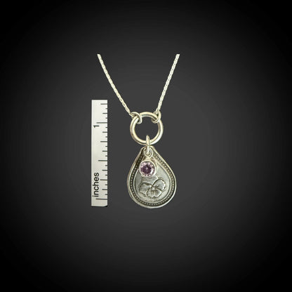 Size reference of February violet birth flower sterling silver necklace with amethyst-purple CZ stone next to inch ruler.