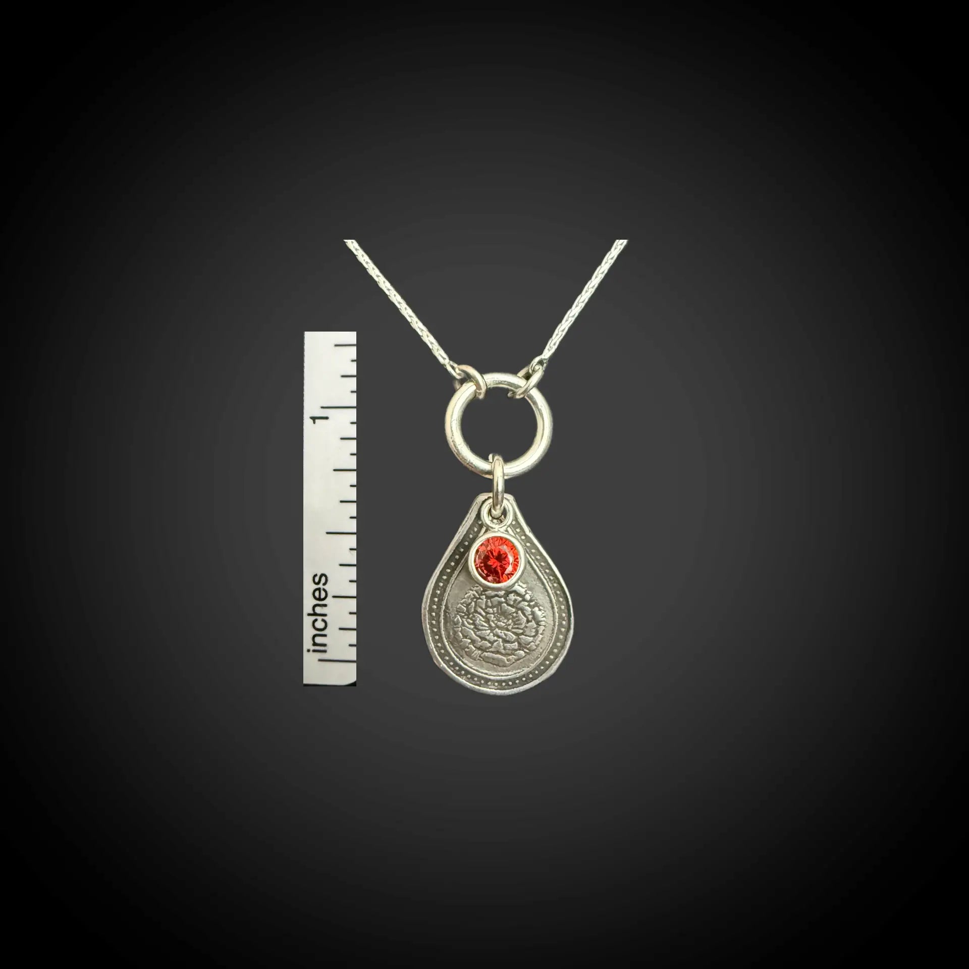 Size reference of January carnation birth flower sterling silver necklace with garnet-red CZ birthstone next to inch ruler.