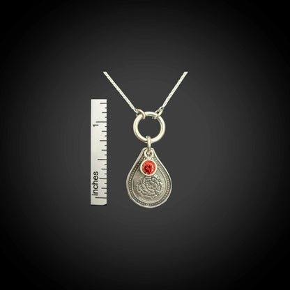 Size reference of January carnation birth flower sterling silver necklace with garnet-red CZ birthstone next to inch ruler.