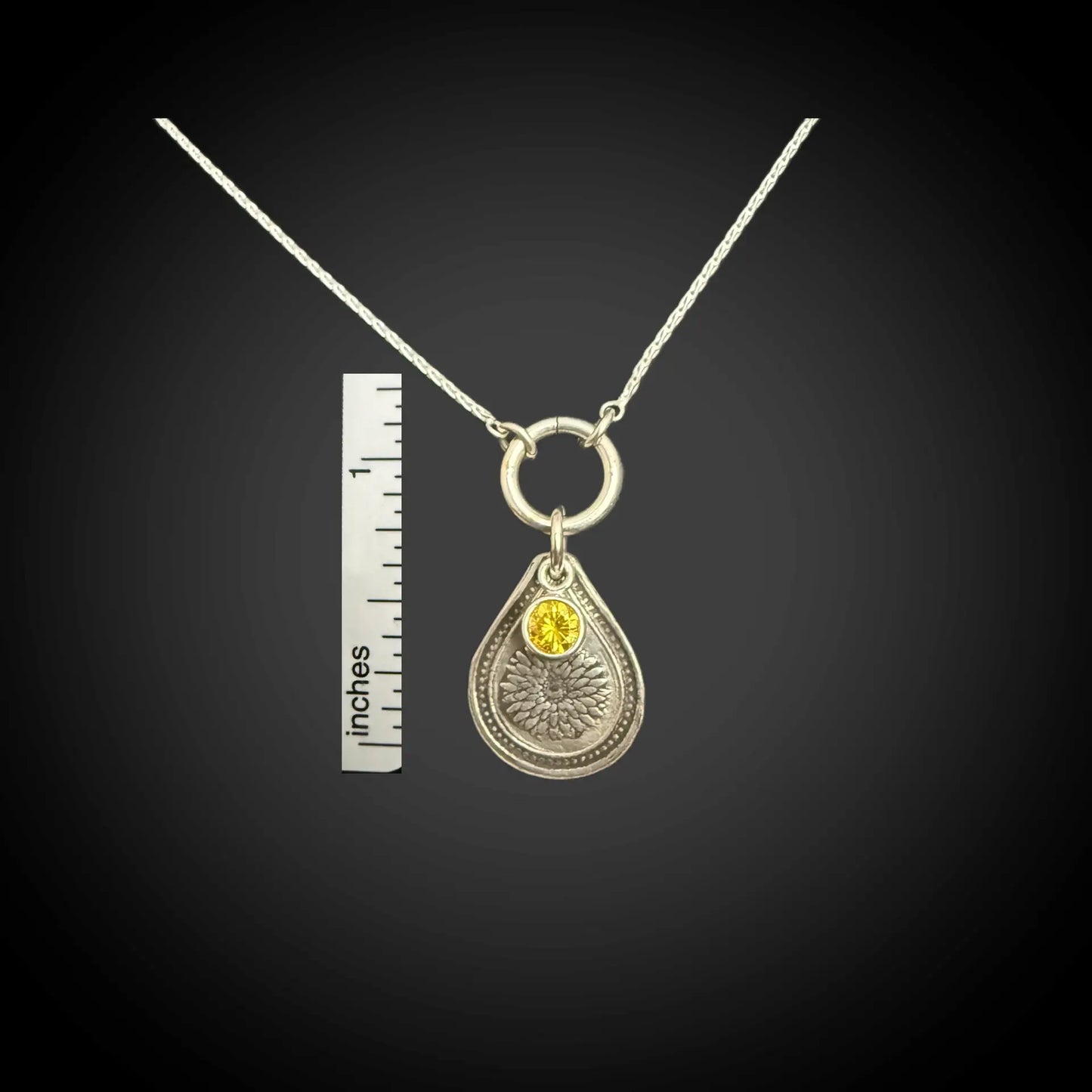 Size reference of November chrysanthemum birth flower sterling silver necklace with golden citrine CZ stone next to inch ruler.