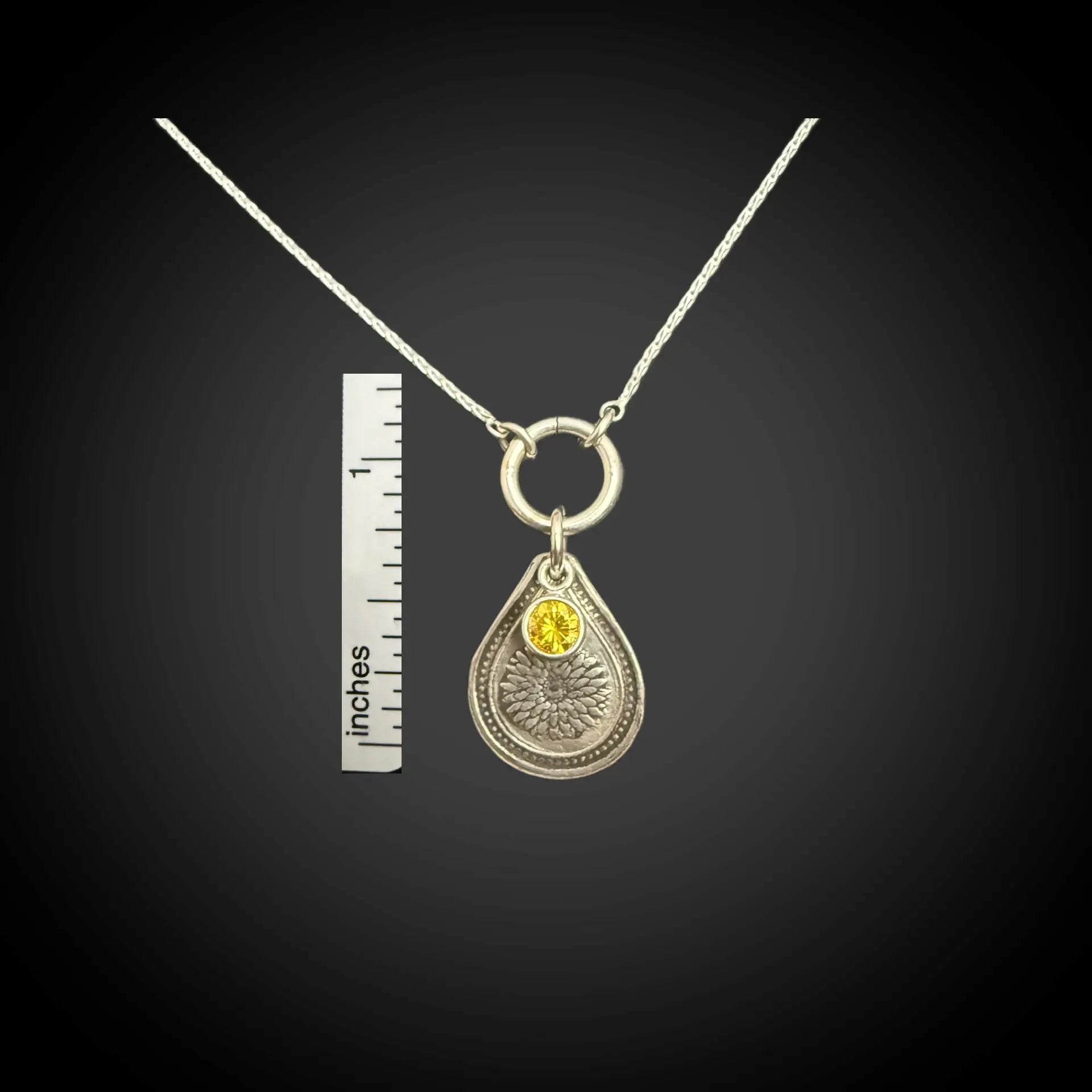 Size reference of November chrysanthemum birth flower sterling silver necklace with golden citrine CZ stone next to inch ruler.