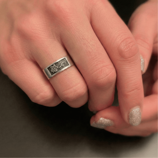 Close-up of a hand wearing a silver ring with intricate design of a March Daffodil birth month flower on a dark background