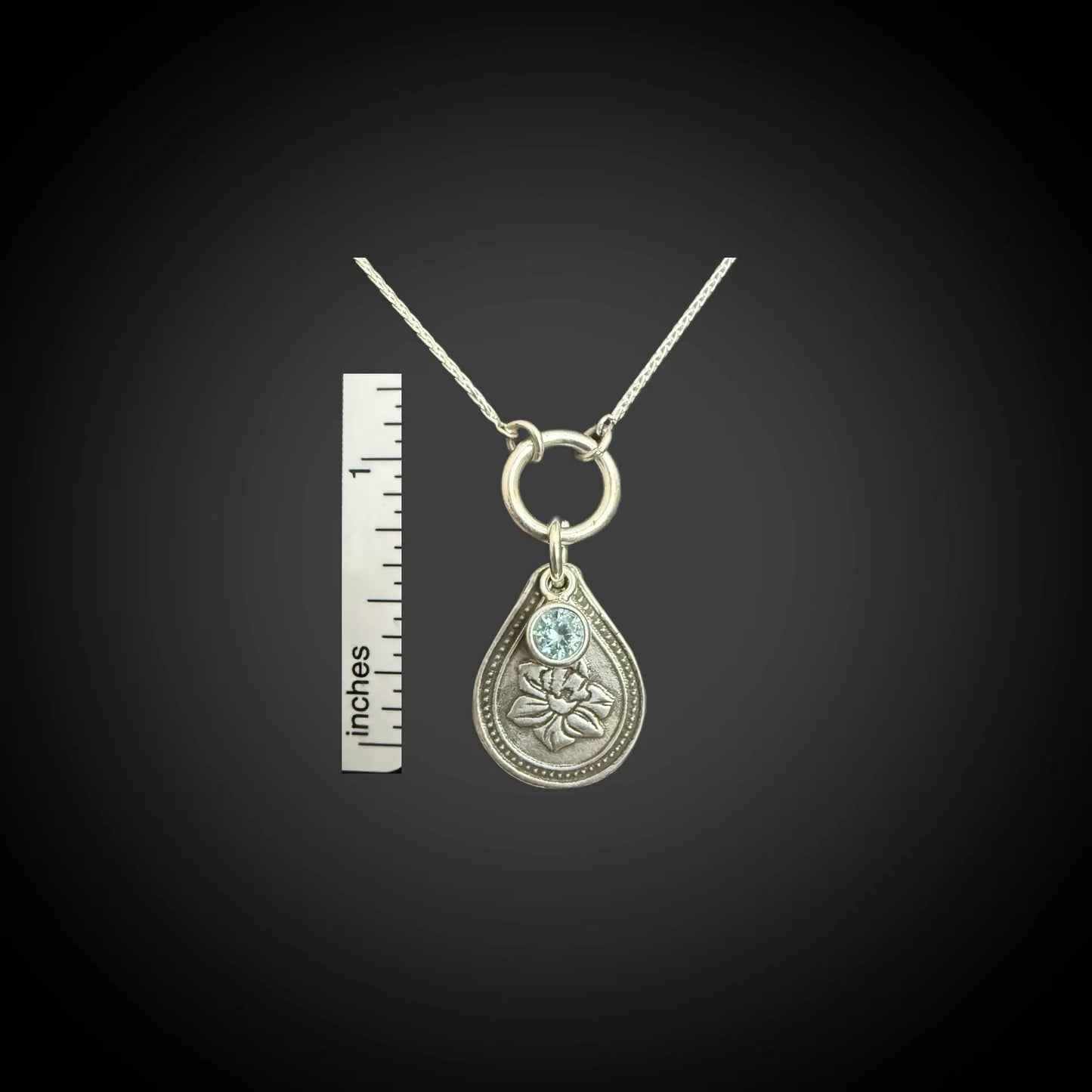 Size reference of March daffodil birth flower sterling silver necklace with aquamarine CZ stone next to inch ruler.
