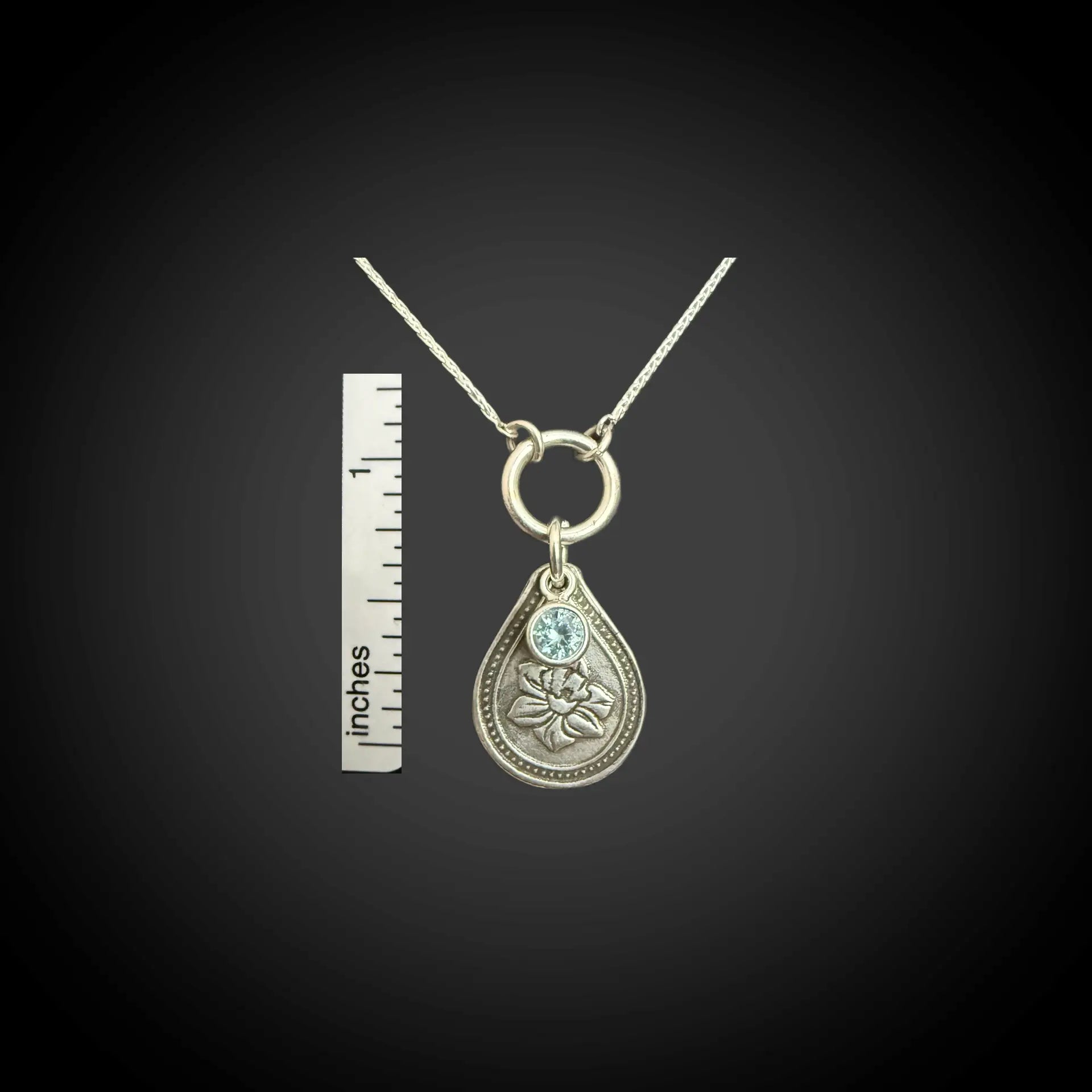 Size reference of March daffodil birth flower sterling silver necklace with aquamarine CZ stone next to inch ruler.