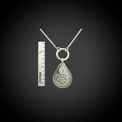 Size reference of March daffodil birth flower sterling silver necklace with aquamarine CZ stone next to inch ruler.