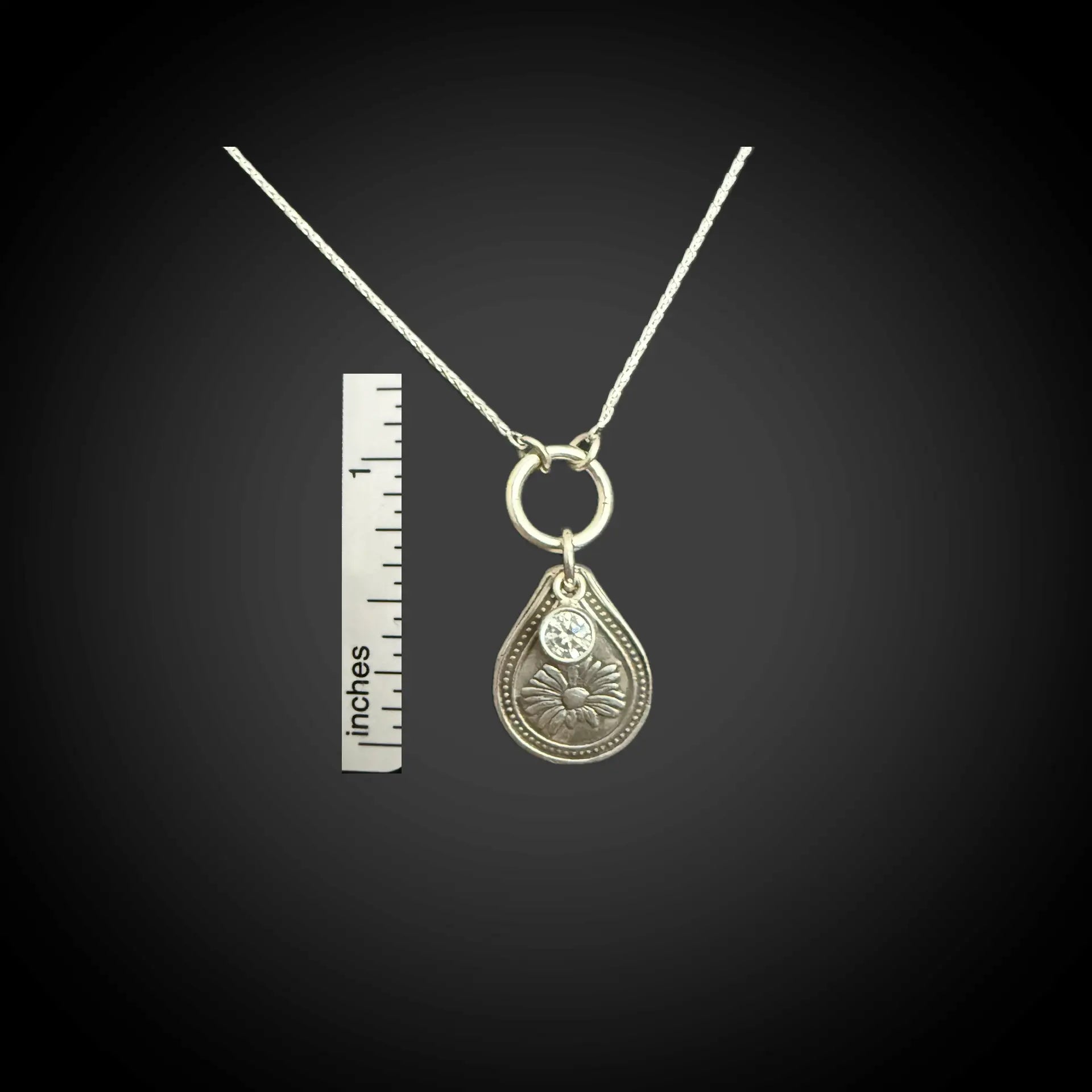 Size reference of April daisy birth flower sterling silver necklace with clear diamond-like CZ stone next to inch ruler.