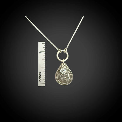 Size reference of April daisy birth flower sterling silver necklace with clear diamond-like CZ stone next to inch ruler.