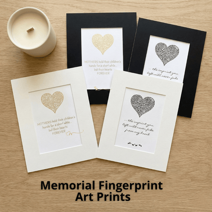 Memorial fingerprint art prints with heart designs on a wooden surface.