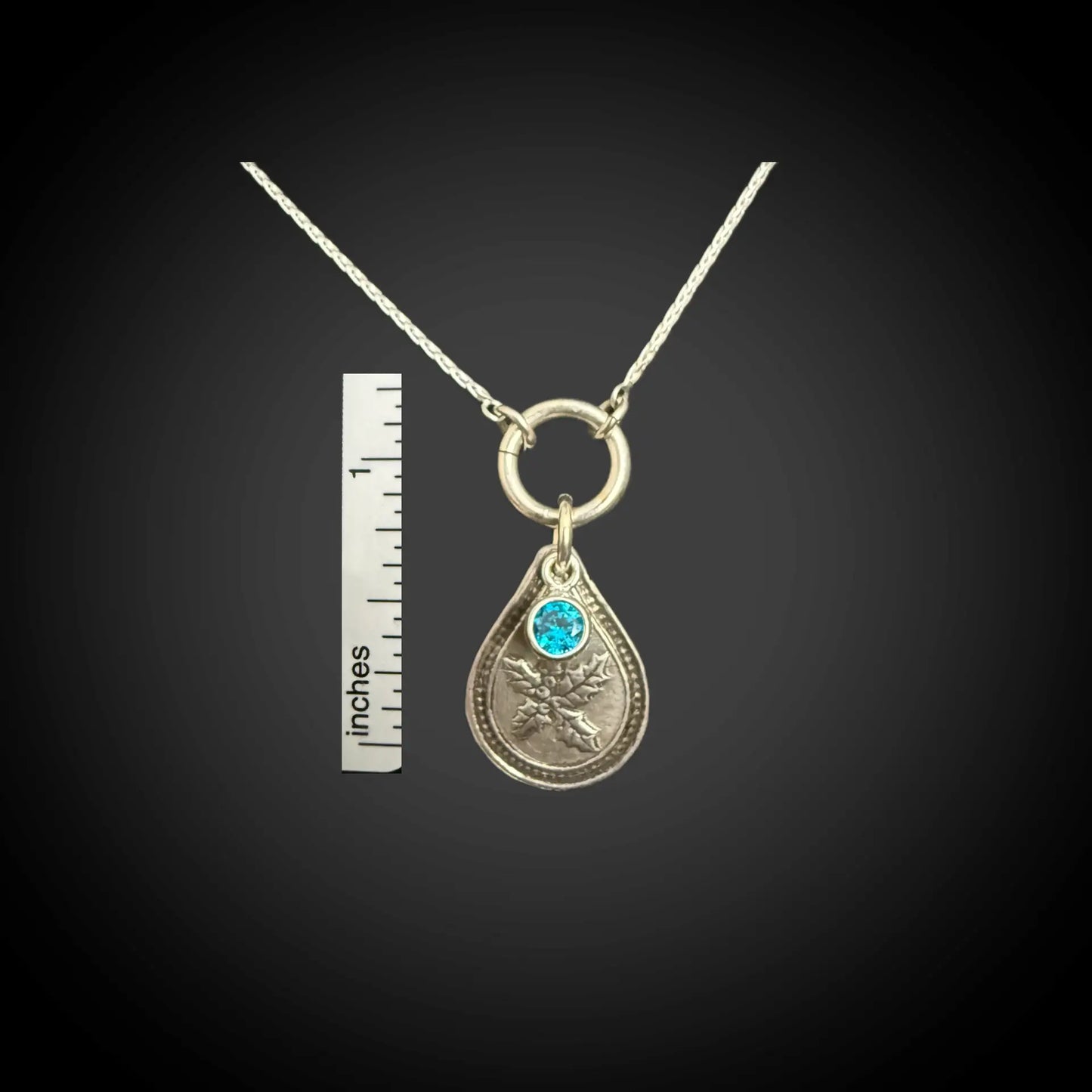 Size reference of December holly birth flower sterling silver necklace with blue zircon CZ stone next to inch ruler.