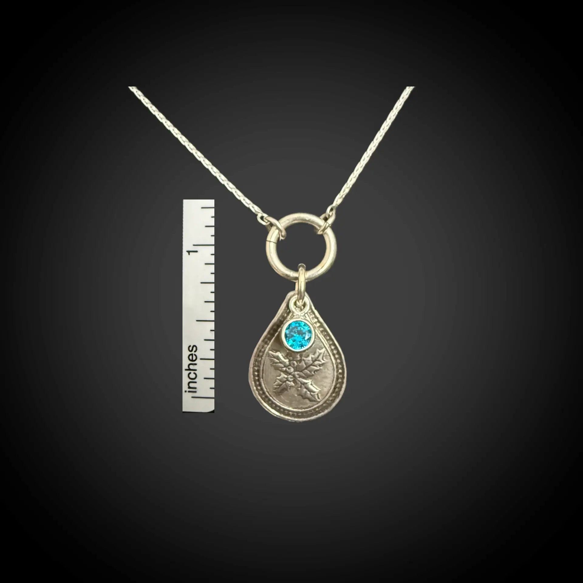 Size reference of December holly birth flower sterling silver necklace with blue zircon CZ stone next to inch ruler.