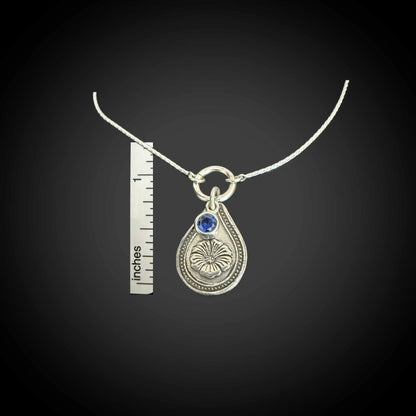 Size reference of September morning glory birth flower sterling silver necklace with sapphire-blue CZ stone next to inch ruler.