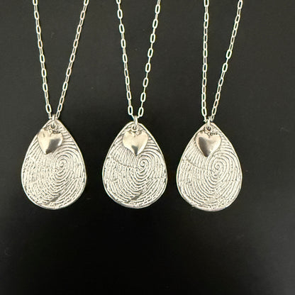 Three silver fingerprint pendants on chains against a black background