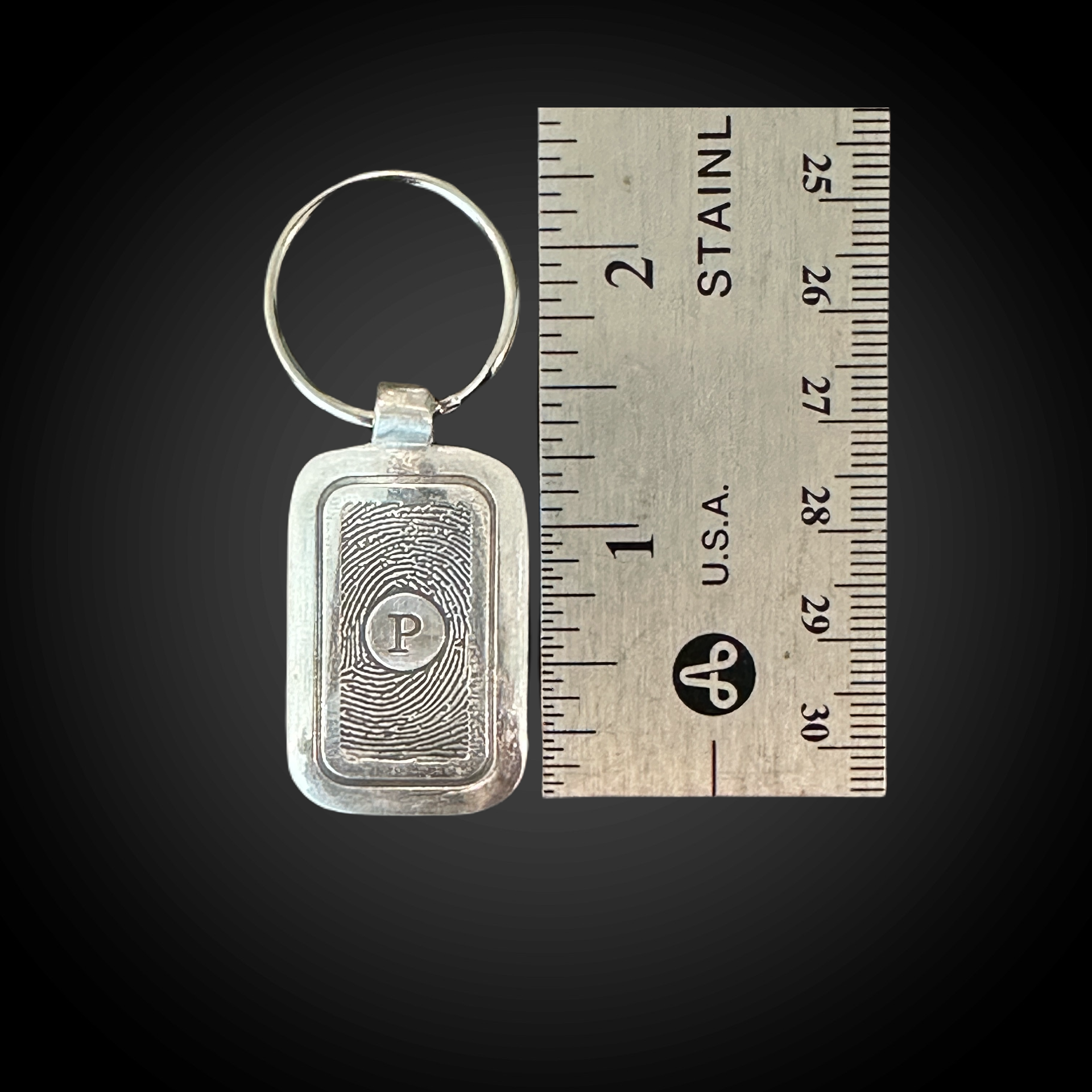 sterling silver rectangle keychain with single initial and fingerprint impression. Shown next to ruler for size.