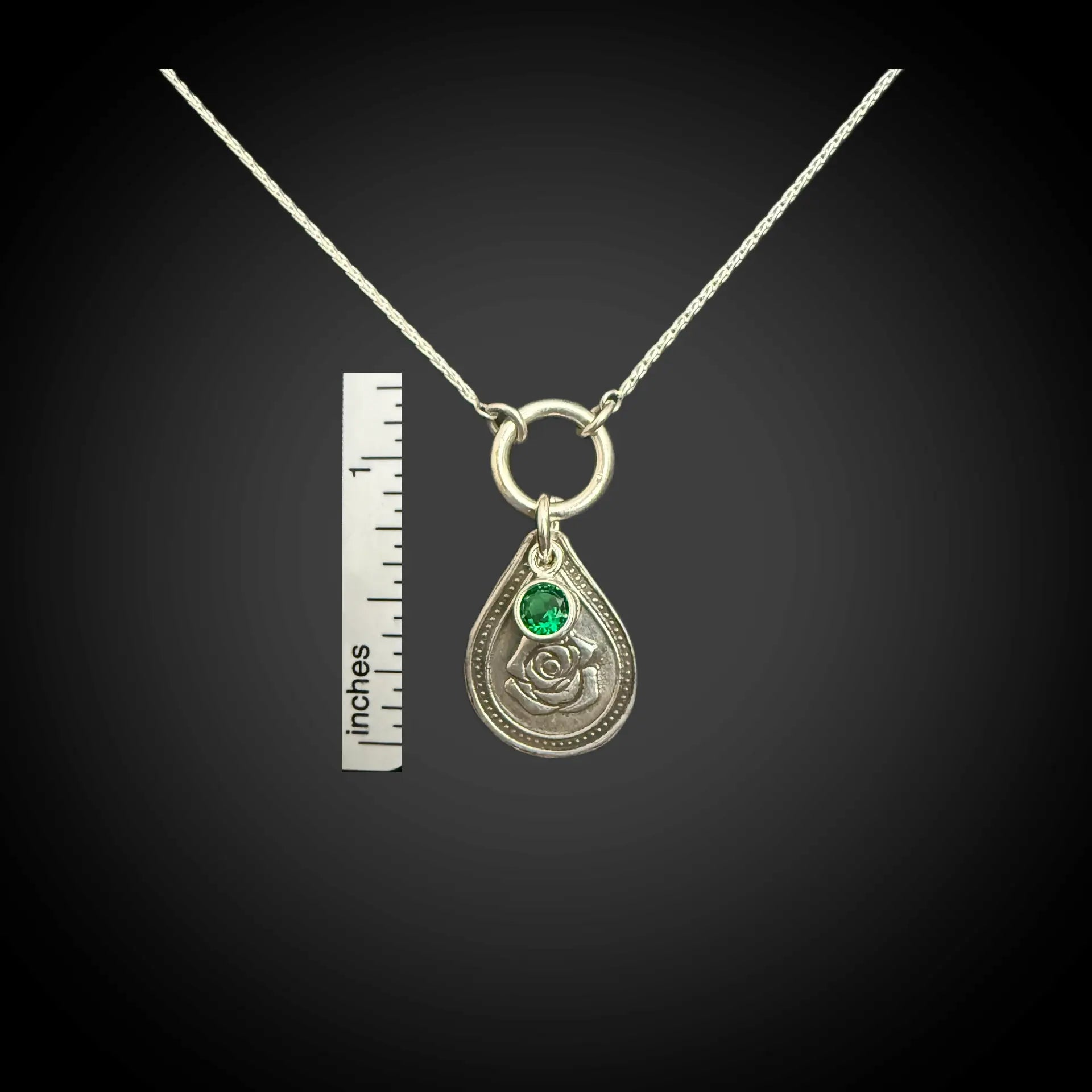 Size reference of June rose birth flower sterling silver necklace with emerald-green CZ stone next to inch ruler.