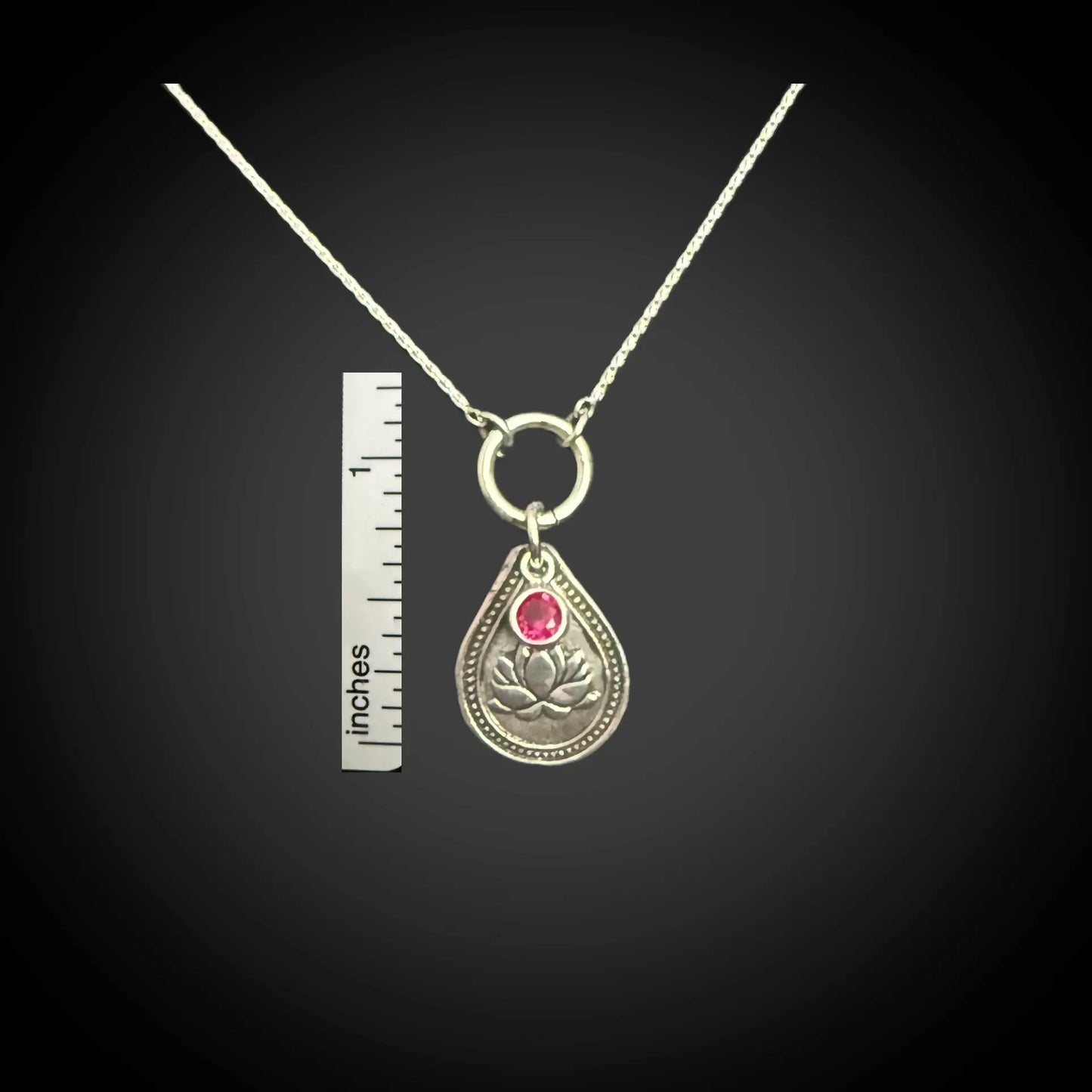 Size reference of July water lily birth flower sterling silver necklace with ruby-red CZ stone next to inch ruler.